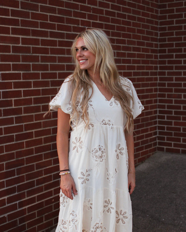 Woman wearing a white floral dress standing against a brick wall.
